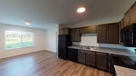 This single-floor unit offers a clean, functional layout with a cohesive design aesthetic throughout. The open-concept kitchen and living area form the heart of the space, where rich, dark-toned shaker-style cabinetry pairs with granite-look countertops and a full suite of black appliances, including a refrigerator, dishwasher, electric range, and over-the-range microwave. A double-basin stainless steel sink sits beneath ample upper and lower cabinet storage. The kitchen flows seamlessly into the living area, which benefits from a large window that draws in natural light and offers outdoor views of green surroundings.

Wood-style plank flooring extends consistently throughout the unit, adding warmth and visual continuity. The bedrooms are well-proportioned, each featuring windows with blinds that frame pleasant outdoor views, and ceiling fans for added comfort. Closets are outfitted with built-in shelving systems for organized storage.

The bathroom is thoughtfully designed with accessibility in mind, featuring grab bars positioned at key locations, a marble-look tile surround in the shower area, and neutral tile flooring. White walls and clean finishes keep the overall atmosphere bright and welcoming throughout the entire space.