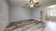 Located at 11440 Old River School Rd in Downey, CA, this efficiently designed single-floor unit offers a thoughtful layout across three functional spaces: a living room, kitchen, and bathroom. The living room is finished with grey-toned laminate wood flooring that runs throughout the unit, complemented by soft blue-grey walls and clean white baseboards. A ceiling fan with an integrated light fixture provides both ventilation and ambient lighting, while a window with security bars allows natural light to filter in and offers views of the surrounding greenery. A wall-mounted heating unit ensures year-round comfort. The kitchen is well-appointed with crisp white shaker-style cabinetry, quartz countertops, and a striking mosaic tile backsplash in grey and white tones. Stainless steel appliances, including a gas range and over-the-range microwave, add a modern, functional touch. The bathroom features a clean, contemporary aesthetic with a soaking tub and shower surround clad in large-format marble-look porcelain tile in white and grey veining, lending an elegant feel to the space. Overall, the unit presents a cohesive, modern design with quality finishes that maximize both style and functionality.