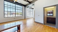 This 1-bedroom, 2-bathroom unit at 101 E Sixth St in Winston-Salem, NC, blends industrial character with modern finishes. The open living area impresses with soaring ceilings, exposed ductwork, and expansive factory-style windows that flood the space with natural light and urban views. Warm hardwood floors run throughout. The kitchen features rich dark cabinetry, granite countertops, stainless steel appliances, a breakfast bar with open shelving, and pendant lighting. The bedroom offers two generous closets with built-in shelving. Both bathrooms include tub/shower combos, tile flooring, and granite-topped vanities.