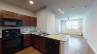 This single-floor residence offers a thoughtfully designed open-concept layout that seamlessly connects the kitchen and living areas. The kitchen is well-equipped with rich dark wood cabinetry, granite-style countertops, a full suite of black appliances including a refrigerator, range, microwave, and dishwasher, and a peninsula with an integrated sink that opens directly to the living space. Hardwood-style flooring flows throughout the main living areas, adding warmth and continuity. The spacious living room features vaulted ceilings, a ceiling fan, recessed and track lighting, and access to a private door, while large windows allow generous natural light to fill the space. Multiple bedrooms are finished with plush carpet, ceiling fans, and bright windows that bring in natural light and neighborhood views. The bathrooms are clean and functional, featuring wood-style flooring, dark wood vanities, and a full tub-shower combo with built-in shelving. Additional highlights include a walk-in closet with wire shelving for ample storage, and a wide hallway corridor that connects all areas of the home efficiently. The overall aesthetic is neutral and modern, offering a versatile canvas for a variety of interior styles.