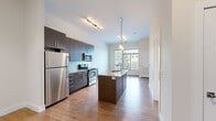 This well-appointed 1-bedroom, 1-bathroom unit at 900 Luxor Ln in Norristown, PA offers a thoughtfully designed layout across a single floor. The open-concept living and dining area flows seamlessly into a modern kitchen, which serves as the centerpiece of the space. The kitchen features dark espresso cabinetry reaching floor to ceiling, granite countertops, a central island with a built-in sink and pendant lighting, and a full suite of stainless steel appliances including a refrigerator, electric range, and over-the-range microwave. Warm hardwood flooring extends throughout the main living areas, complemented by neutral walls and clean white trim. Large windows in the dining area invite abundant natural light and provide outdoor views of surrounding greenery. The bedroom is carpeted for comfort and is brightened by dual windows with outdoor views, creating an airy, relaxed atmosphere. A spacious walk-in closet with wrap-around wire shelving offers generous storage. The bathroom is finished with light tile flooring and includes a tub-shower combination enclosed by sliding glass doors. A connecting hallway with hardwood flooring ties each room together, completing this clean, modern, and functional living space.