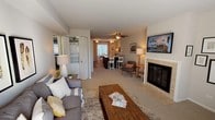 This single-floor residence offers a thoughtfully designed layout with a comfortable, neutral aesthetic throughout. The open living area serves as the heart of the home, featuring a tile-surround fireplace with glass doors topped by a wall-mounted television. Large sliding glass doors flood the space with natural light, while a ceiling fan adds practicality. The living area flows naturally into a dining space with bar-height seating, creating an ideal setting for both relaxing and entertaining.

The kitchen is outfitted with rich dark cabinetry, granite-style countertops, black appliances, a mosaic tile backsplash, and hardwood-style flooring. A convenient walk-in pantry or storage closet is directly accessible from the kitchen.

The primary bedroom is generously sized with plush carpet, a large window, and a spacious closet. A second bedroom provides comfortable accommodations with its own window and closet storage. Both bathrooms feature granite-style vanity countertops; one includes a tub-shower combination, while the other offers a separate shower alongside a soaking tub. A stacked washer/dryer unit is conveniently tucked behind bi-fold doors within the unit.