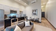 Located at 111 S Greenwood Ave in Tulsa, Oklahoma, this thoughtfully designed single-floor unit makes excellent use of its intimate footprint. Soaring ceilings throughout create a striking sense of verticality and openness that elevates the entire space.

The open-concept living and kitchen area serves as the heart of the unit. The kitchen is outfitted with stainless steel appliances, including a range, microwave, and refrigerator, paired with crisp white upper cabinetry and dark lower cabinetry for a modern two-tone contrast. A compact dining nook sits adjacent, ideal for casual meals. The living area accommodates comfortable seating and benefits from tall windows dressed in sheer curtains that invite abundant natural light. A wall-mounted mini-split HVAC system provides climate control with a clean, modern profile.

The bedroom is a calm, well-proportioned retreat with neutral walls and high ceilings that amplify the sense of space. Light wood-toned flooring runs throughout the main areas, adding warmth and continuity.

The bathroom features a clean, contemporary design with hexagonal white floor tile, a floating vanity with gold fixtures, a large mirror, and a full toilet. A sliding barn-style door adds an industrial-modern touch. The overall ambiance of the unit is modern and refined, with a neutral palette and curated finishes that balance style and functionality.
