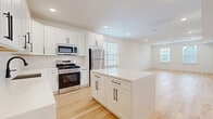 Located at 325-327 Union Blvd in Totowa, NJ, this well-appointed 2-bedroom, 2-bathroom single-floor unit offers a thoughtfully designed layout with modern finishes throughout. Light hardwood flooring flows seamlessly across every room, complementing the bright, neutral white walls and recessed lighting that create a clean, contemporary aesthetic.

The open-concept kitchen is a standout feature, showcasing white shaker-style cabinetry with matte black hardware, a white quartz center island, and a full suite of stainless steel appliances including a gas range, over-the-range microwave, dishwasher, and refrigerator. The kitchen opens directly into the combined dining and living area, which is bathed in natural light from multiple windows with blinds.

The spacious primary bedroom features dual windows and connects to a generously sized walk-in closet with built-in shelving and hanging rods. The second bedroom also benefits from natural light through a large window. A hallway connects the living areas to three closets total, two bathrooms, and an in-unit laundry area. The bathrooms are finished with large-format grey tile flooring, white vanities, and a tub-shower combination with sliding glass doors and matte black fixtures.