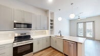 Located at 8157 Ederville Rd in Fort Worth, TX, this 1-bedroom, 1-bathroom unit offers a thoughtfully designed layout that maximizes its comfortable footprint. Light wood-tone flooring flows throughout the main living areas, complemented by neutral walls and clean lines that create a bright, modern ambiance.

The kitchen and living area form an open, functional space. The kitchen is equipped with stainless steel appliances — including a side-by-side refrigerator with ice and water dispenser, a range, and a microwave — paired with soft gray shaker-style cabinetry, white countertops, and a subtle tile backsplash. Natural light filters through windows and sliding glass doors that open to a private balcony with views of the surrounding area, complete with a ceiling fan overhead.

The bedroom is carpeted for comfort and features a large window that brings in ample natural light. The full bathroom offers a well-appointed vanity with gray cabinetry and a white countertop, a soaking tub with marble-style tile surround, and direct access to a generously sized walk-in closet outfitted with built-in shelving and hanging rods, providing excellent storage and organization.