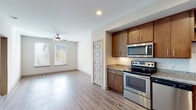 This single-floor residential unit offers a thoughtfully designed layout that balances functionality and comfort. The kitchen is a standout feature, equipped with rich warm-toned cabinetry, granite countertops, a white subway tile backsplash, and a full suite of stainless steel appliances including an electric range, over-the-range microwave, dishwasher, and refrigerator. Recessed lighting and wood-look plank flooring throughout the kitchen and living areas add a clean, modern aesthetic.

The open living area flows naturally from the kitchen, bathed in natural light from double windows fitted with horizontal blinds. A ceiling fan overhead provides year-round comfort in this space. The transition from the main living area to the bedroom is smooth, with the bedroom offering plush carpeting, a ceiling fan with integrated lighting, and a window that lets in ample natural light.

The bathroom is well-finished, featuring a tub-shower combination with white subway tile surround, a granite-topped vanity with an undermount sink, brushed nickel hardware, and tile flooring. Throughout the unit, consistent design choices—granite surfaces, warm wood cabinetry, and neutral wall tones—create a cohesive and inviting atmosphere.