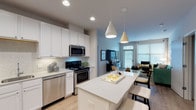 This well-appointed single-floor residence offers a thoughtfully designed open-concept layout that seamlessly connects the kitchen, dining, and living areas. The kitchen is a standout feature, showcasing crisp white shaker cabinets extending to the ceiling, light quartz countertops, a classic tile backsplash, and a full suite of stainless steel appliances including a gas range, built-in microwave, dishwasher, and refrigerator. A large center island with seating provides an ideal space for casual dining and entertaining. Pendant lighting and recessed fixtures illuminate the space with a warm, modern ambiance. The living room is bright and welcoming, benefiting from large windows and a sliding glass door that invite an abundance of natural light. Light hardwood-style flooring flows throughout the main living areas, adding warmth and continuity. The two bedrooms are comfortable retreats, each with plush carpeting, generous windows with blinds, and ample room for furnishings. The primary bathroom features a dual-sink vanity with white cabinetry and large-format tile flooring, while the second bathroom offers a soaking tub with elegant marble-style tile surround. The overall aesthetic is clean, contemporary, and move-in ready.