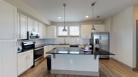 This two-story, 2-bedroom, 2.5-bathroom home delivers a thoughtfully designed layout with modern finishes throughout. The main level features an open-concept living area with warm wood-look flooring, a ceiling fan, and a pendant light that anchors the space. The kitchen is a standout, showcasing crisp white shaker cabinetry, dark granite countertops, a classic subway tile backsplash, and a full suite of stainless steel appliances including a GE side-by-side refrigerator with ice and water dispenser, a range, microwave, and dishwasher. A central island with seating provides additional prep and dining space, while multiple windows invite natural light. A half bathroom on the main level features white cabinetry with dark granite counters and wood-look flooring. Carpeted staircase leads to the upper level, where the bedrooms offer plush carpet flooring and generous windows with outdoor views. The full bathrooms upstairs are finished with white subway tile tub-and-shower surrounds, white vanities with dark granite countertops, large mirrors, and wood-look tile flooring. The home's consistent use of neutral tones, quality materials, and modern fixtures creates a cohesive and inviting atmosphere throughout both floors.
