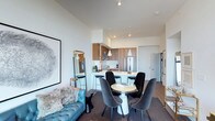 Located at 300 1st in San Diego, this Model Plan A residence on the 15th floor presents a thoughtfully designed single-floor layout that maximizes both function and style. The open-concept living, dining, and kitchen area serves as the heart of the home, creating a cohesive and inviting atmosphere throughout.

The kitchen features warm wood cabinetry, stainless steel appliances, and a sleek peninsula with bar seating — ideal for casual dining or entertaining. Pendant lighting with clean, contemporary silhouettes hangs above, adding a refined touch to the space. The kitchen flows naturally into the dining area, which is anchored by a round pedestal table surrounded by plush upholstered chairs, creating an intimate setting for meals.

The living area is bright and open, highlighted by soaring ceilings and crisp white walls that enhance the sense of space. A tufted blue sofa anchors the lounge area alongside curated décor, including a large-scale framed artwork. Durable wood-tone flooring transitions seamlessly through the common areas, while plush carpet adds warmth to the living zone. The overall design balances modern aesthetics with comfortable, livable details, making this a well-appointed San Diego residence.