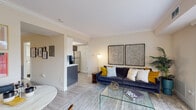This single-floor residence is thoughtfully designed with a contemporary aesthetic that balances functionality and style. The open-concept living and dining area serves as the heart of the home, featuring light wood-tone flooring, crown molding, and warm neutral walls. A navy velvet sofa, glass coffee table, and curated wall art anchor the living space, while a dining area with a round marble-top table sits adjacent. Large sliding glass doors flood the space with natural light and provide direct access to an outdoor balcony overlooking greenery.

The kitchen is outfitted with high-gloss upper cabinetry in white, contrasting grey lower cabinets, crisp white countertops, under-cabinet lighting, a stainless steel undermount sink, and a black dishwasher — combining a clean, modern look with practical utility.

The primary bedroom is generously sized, accommodating a full bedroom suite with dresser, open shelving unit, and an oval mirror accent. It features crown molding, soft neutral tones, and an open-concept passage to additional storage. The second bedroom includes a large built-in wardrobe and a window with outdoor views, providing ample natural light and closet space. The overall ambiance is modern, cohesive, and move-in ready.