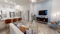 This well-designed single-floor residence offers a thoughtfully laid-out open-concept floor plan that seamlessly connects the main living spaces. The living room is anchored by soaring ceilings, light wood-style flooring, and large windows that invite natural light, creating an airy and welcoming atmosphere. A ceiling fan adds both comfort and style overhead, while ample wall space accommodates a media console and entertainment setup.

The kitchen is outfitted with white shaker-style cabinetry extending to the upper walls for generous storage, granite-look countertops, and a full suite of stainless steel appliances including a refrigerator, range, and over-the-range microwave. A breakfast bar with seating connects the kitchen to the living area, enhancing the open layout.

In-unit laundry is conveniently accessible, adding everyday practicality to the space. The bedroom is a calm retreat, featuring plush carpet flooring, windows with natural light, and ample room for furnishings. The bathroom is finished with granite countertops, white cabinetry, a large vanity mirror, and a full shower-tub combination, all carried out in a clean, neutral palette.

Throughout, the consistent use of light tones, modern fixtures, and quality finishes creates a cohesive, contemporary living environment.