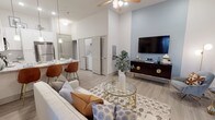 This well-designed single-floor residence offers a thoughtfully laid-out open-concept floor plan that seamlessly connects the main living spaces. The living room is anchored by soaring ceilings, light wood-style flooring, and large windows that invite natural light, creating an airy and welcoming atmosphere. A ceiling fan adds both comfort and style overhead, while ample wall space accommodates a media console and entertainment setup.

The kitchen is outfitted with white shaker-style cabinetry extending to the upper walls for generous storage, granite-look countertops, and a full suite of stainless steel appliances including a refrigerator, range, and over-the-range microwave. A breakfast bar with seating connects the kitchen to the living area, enhancing the open layout.

In-unit laundry is conveniently accessible, adding everyday practicality to the space. The bedroom is a calm retreat, featuring plush carpet flooring, windows with natural light, and ample room for furnishings. The bathroom is finished with granite countertops, white cabinetry, a large vanity mirror, and a full shower-tub combination, all carried out in a clean, neutral palette.

Throughout, the consistent use of light tones, modern fixtures, and quality finishes creates a cohesive, contemporary living environment.