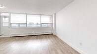 Located on the 18th floor at 55 Triller Ave in Toronto's Roncesvalles neighbourhood, this one-bedroom, one-bathroom unit offers a well-designed layout with modern finishes throughout. Light wood laminate flooring runs continuously across the entire space, complementing the clean white walls and creating a bright, cohesive aesthetic.

The open-concept kitchen and living area forms the heart of the unit. The kitchen is outfitted with white shaker-style cabinetry, grey subway tile backsplash, dark countertops, and a full suite of stainless steel appliances including a refrigerator, electric range, over-the-range microwave, and dishwasher. A peninsula with additional counter space provides a natural division between the kitchen and the open living area.

The living room benefits from expansive floor-to-ceiling windows that flood the space with natural light and frame sweeping views of the Toronto skyline and waterfront — a standout feature of this high-floor unit. Baseboard heating runs beneath the windows throughout.

The spacious primary bedroom also enjoys generous window coverage with broad city views and includes a mirrored sliding-door closet. The bathroom features a full soaking tub finished with classic white subway tile surrounds and chrome fixtures, offering a clean, timeless look.