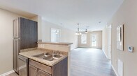 Located at 6306 Old Mooretown Rd in Williamsburg, Virginia, this two-bedroom, two-bathroom residence offers a practical and comfortable single-floor layout. The open-concept living and kitchen area forms the heart of the home, where durable hardwood-style flooring, neutral warm-toned walls, and ceiling fans create a bright and welcoming atmosphere. The kitchen is well-appointed with dark espresso cabinetry, granite-style countertops, stainless steel appliances including a French door refrigerator and electric range, and a peninsula with a double sink that opens to the living space — ideal for both cooking and entertaining. Natural light pours into the living room through a glass door, adding to the airy feel of the space. The primary bedroom is generously sized with plush carpeting, a ceiling fan, and windows that bring in ample daylight. The second bedroom mirrors this comfortable aesthetic. Each bathroom is clean and functional, with one featuring a modern floating vanity, sleek tile flooring, and contemporary lighting. Two dedicated closets provide practical storage solutions throughout. The overall design is cohesive and move-in ready, offering a comfortable lifestyle in a well-maintained Williamsburg community.