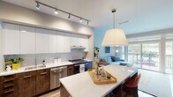 This well-appointed single-floor residence showcases a cohesive modern design with high-quality finishes throughout. The open-concept kitchen is a standout feature, boasting two-tone cabinetry with rich walnut lower cabinets and gloss white upper cabinets, pristine white quartz countertops, a subway tile backsplash, and a full suite of stainless steel appliances including a French door refrigerator, built-in microwave, dishwasher, and range. A large kitchen island with pendant lighting anchors the space and flows seamlessly into the dining and living areas. The living room is bright and welcoming, with access to an outdoor balcony that brings in natural light and outdoor views. Light wood-tone flooring runs throughout the main living areas, adding warmth to the contemporary palette. The primary bedroom features plush carpeting, a walk-in closet, and a private en-suite bathroom. The bathrooms are finished with dark tile flooring, walnut vanity cabinetry, white quartz countertops, and large illuminated mirrors. Additional bedrooms are comfortably sized with soft carpeting and neutral walls. Track lighting and recessed fixtures provide well-distributed illumination throughout the residence, completing the clean, modern aesthetic.