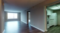 This 2-bedroom, 2-bathroom residence is thoughtfully designed across a single floor, offering a functional and cohesive layout. The open living and dining areas are finished with dark hardwood-style flooring that runs throughout the main spaces, complemented by neutral gray walls and textured ceilings. Natural light enters through large windows, with city views visible from both bedrooms, adding a dynamic urban backdrop to the space.

The kitchen features white cabinetry with brushed nickel hardware, granite-style countertops, a stainless steel sink, and a mosaic tile backsplash that introduces subtle visual interest. Both bedrooms are generously sized and finished with plush, light-toned carpeting, creating a comfortable contrast to the hard floors in the common areas. Each room benefits from large sliding windows framing urban skyline views.

The two bathrooms are finished with white tile flooring and clean, neutral tiling throughout. The first bathroom includes a full tub and shower with a rain showerhead and chrome fixtures, while the second features a glass-enclosed walk-in shower, a floating vanity, and ample mirror space. Together, the rooms present a clean, move-in-ready aesthetic suited for modern urban living.