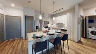 Located at 13103–13121 Honore Ave in Osprey, Florida, this single-story residence offers a thoughtfully designed open-concept layout that seamlessly connects the kitchen, dining, and living areas. The kitchen is a standout feature, showcasing light wood-grain cabinetry, granite countertops, stainless steel appliances, and a large center island with bar seating for multiple guests—all illuminated by stylish pendant lighting and a track light fixture above. Rich wood-look flooring flows throughout the main living areas, complementing the clean, neutral color palette. The living room is bright and welcoming, with crown molding, a ceiling fan, and large windows and a glass door that invite generous natural light. The bedrooms are carpeted for comfort, each equipped with a ceiling fan, ample natural light from well-sized windows, and convenient access to closet space. The bathrooms feature granite-topped vanities with wood-toned cabinetry and tub-shower combinations with tile surrounds. An in-unit Whirlpool washer is also present, adding everyday convenience. Overall, the space presents a contemporary, cohesive aesthetic with quality finishes throughout.
