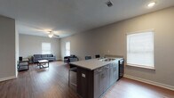 This single-floor residence offers a clean, contemporary design with a cohesive aesthetic carried throughout every room. Rich hardwood-style flooring runs continuously across the entire unit, grounding the space with warmth and visual continuity. Neutral gray walls create a versatile backdrop that complements the modern finishes found throughout.

The open-concept kitchen and living area serves as the heart of the home. The kitchen is equipped with black appliances, including a full-size refrigerator, range, and over-the-range microwave, alongside light wood cabinetry and granite-style countertops. A central island with bar seating provides additional workspace and casual dining. The adjacent living area is generously sized, featuring vaulted ceilings, a ceiling fan, and multiple windows that allow natural light to fill the space.

The bedrooms are comfortably proportioned, each outfitted with ceiling fans and access to closet space. The clean, understated design of each room provides a flexible foundation for personalization. Two bathrooms serve the unit, both featuring dark wood vanities with granite-style countertops, framed mirrors, and chrome fixtures. One bathroom includes a shower-tub combination, while the other offers a standalone shower. The overall layout is functional and well-organized, making efficient use of the available space.