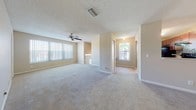 This single-floor residence offers a thoughtfully designed layout with a warm, neutral color palette throughout. The expansive main living area is a standout feature, characterized by plush wall-to-wall carpeting, a textured ceiling, and a ceiling fan that promotes airflow and comfort. Large windows dressed with vertical blinds allow generous natural light to fill the space, while a staircase railing detail adds an architectural accent to the open floor plan. The living area connects seamlessly to additional rooms via a central hallway, enhancing the home's functional flow.

The bedrooms continue the home's consistent aesthetic, each featuring soft carpeted floors, ceiling fans, and built-in closets with sliding or bifold doors. One bedroom includes a connected en-suite bathroom, providing added privacy and convenience. An additional half bathroom is finished with wood-toned cabinetry, a stone-topped vanity, and hardwood flooring, offering a polished look.

A dedicated in-unit laundry room accommodates a full-size washer and dryer, complete with overhead shelving for storage. Throughout the home, clean white trim, neutral beige walls, and an abundance of windows create a bright, cohesive, and move-in-ready environment.
