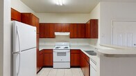 This single-story residence offers a practical and cohesive layout across its main living areas. The kitchen is designed in a U-shaped configuration, featuring rich medium-toned wood cabinetry extending from floor to ceiling, providing generous storage space. Light-colored countertops complement the cabinetry, while white appliances — including a refrigerator, electric range with overhead ventilation hood, and dishwasher — are neatly integrated throughout. Light ceramic tile flooring runs throughout the kitchen, contributing to a clean, easy-to-maintain environment.

The living area is carpeted and bathed in natural light from a large window, with a ceiling fan overhead and a door providing direct outdoor access. The neutral wall tones and open feel of the space lend a calm, airy ambiance. Multiple bedrooms follow a similar design language, each featuring plush carpet, ceiling fans with light fixtures, and windows that allow in natural daylight.

The bathrooms maintain consistency with the rest of the unit through matching wood vanity cabinetry, light countertops, tile flooring, and tiled tub-shower combinations. Large mirrors above the vanities enhance the sense of space. Overall, the unit presents a cohesive, functional aesthetic throughout.