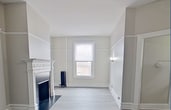 This 500 square foot, one-bedroom apartment in Troy, NY, seamlessly combines historic charm with modern amenities. The living room serves as the heart of the home, featuring a decorative fireplace with an ornate white mantel, adding character to the space. Light gray walls and pristine white trim create a bright, airy atmosphere throughout.

The apartment boasts newly installed gray wood-look flooring, which unifies the space and adds a contemporary touch. Large windows in the living room and bedroom allow for ample natural light, while providing views of the surrounding area. The bedroom, measuring 80 square feet, offers a cozy retreat with a window and wall-mounted light fixture.

The kitchen, though compact, is efficiently designed with wooden cabinets, granite countertops, and a full-sized electric range. A window above the sink brings in natural light. The bathroom features a modern update with sleek marble-look tiling and a white vanity.

Unique architectural elements include high ceilings with picture rail moldings and a ceiling fan in the living area. The apartment's layout is enhanced by a hallway connecting the rooms, adding to the sense of space. Exposed pipes and a vintage radiator nod to the building's history while maintaining functionality.

This unit, located at 17 State St, Unit 5A, offers a perfect blend of historical architecture and modern conveniences, ideal for those seeking a charming urban living space in Troy.