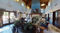 Located at 45418 Howe Rd in San Diego, the Mill Corn Clubhouse is a single-story community gathering space designed with elegance and warmth. The entryway sets an inviting tone with natural stone tile flooring, rich dark wood trim, tall ceilings, and decorative accents including a large round mirror and ornamental vases. French-style glass doors with dark wood frames provide a seamless transition into the main areas of the clubhouse.

The heart of the space is a grand great room featuring soaring vaulted ceilings with exposed, richly stained wood beam detailing. A dramatic floor-to-ceiling stone fireplace serves as the room's focal point, framed by a bold teal accent wall and topped with a mounted flat-screen television. Multiple seating arrangements with wood and upholstered furniture are arranged throughout, complemented by pendant lighting and wall sconces that cast a warm glow. Tall windows and French doors along the walls allow abundant natural light and provide views of the outdoor surroundings.

The clubhouse also includes a well-appointed full kitchen featuring dark wood cabinetry, granite countertops, a mosaic tile backsplash, stainless steel appliances including a double wall oven and dishwasher, and stone tile flooring — offering full functionality for events and catering needs.