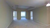 This single-floor home offers a thoughtfully designed layout with an open, airy feel throughout. The centerpiece of the main living area is a striking tray ceiling, which adds architectural depth and visual interest to the space. Neutral beige walls provide a versatile backdrop that complements a wide range of furnishing styles, while soft, plush carpeting underfoot contributes to a comfortable and inviting atmosphere.

Large windows allow natural light to filter generously into the space, brightening the interior and creating a warm, welcoming ambiance. The open floor plan connects the main living area to adjacent rooms, offering both visual flow and functional flexibility. Multiple doorways lead to additional rooms, suggesting a well-organized and connected layout ideal for everyday living.

The clean lines of the architecture, combined with the tray ceiling detail and consistent neutral color palette, give the home a polished yet approachable character. Ample wall space and room dimensions provide practical versatility for furniture arrangement and interior customization. Overall, this home presents a move-in ready environment with classic design elements and a bright, open feel that makes it both comfortable and adaptable.