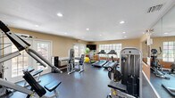 This 420 square foot fitness center is a well-designed space that caters to various workout needs. The room features a dark gray rubberized floor, providing excellent traction and shock absorption for exercise activities. The walls are painted in a warm beige tone with a contrasting orange wainscoting, creating a vibrant yet inviting atmosphere.

The space is illuminated by recessed lighting and benefits from natural light streaming through multiple French doors, enhancing the open feel of the room. These doors also offer potential outdoor views and access.

The gym is equipped with a comprehensive range of exercise machines, including treadmills, weight machines, and resistance training equipment. Colorful exercise balls and other fitness accessories are available, adding versatility to workout options. A wall-mounted TV provides entertainment or instruction possibilities.

A notable feature is the large mirror on one wall, useful for form checking during exercises. Adjacent to the main workout area, there's a connected lounge space visible through a large window, offering a rest area or additional functional space.

The layout is well-organized, allowing for efficient use of the available square footage while maintaining ample space for movement between equipment. This thoughtfully designed fitness center provides a conducive environment for a wide range of physical activities and exercise routines.