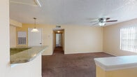 This single-floor residence offers a practical and comfortable layout designed for everyday living. The open living area is finished with plush brown carpet and features a textured ceiling, ceiling fan with integrated lighting, and a half-wall partition that defines the space while maintaining an open feel. Vertical blinds on the windows allow for adjustable natural light throughout. A hallway connects the main living area to the private rooms beyond.

The kitchen is efficiently appointed with white cabinetry, granite-style countertops, tile flooring, a coil-burner electric range with overhead microwave, and pendant lighting — offering a functional workspace that opens toward the living area via a raised breakfast bar counter.

The bedrooms are carpeted and warmly lit, each equipped with ceiling fans and windows with vertical blinds that invite natural light. One bedroom includes louvered bifold closet doors, providing generous storage. Both rooms offer a quiet, comfortable atmosphere.

The two bathrooms share a consistent design language, featuring warm-toned tile flooring, white tub-shower combinations with tiled surrounds, white vanity cabinetry topped with granite-style counters, and well-lit mirrors. Together, they provide functional and clean bathroom spaces suited to daily use.