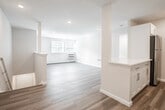 Located at 164 Oakdale Bohemia Rd in Bohemia, NY, this single-floor unit offers a clean, modern aesthetic with thoughtful updates throughout. The open-concept layout connects the living area to the kitchen via a half-wall peninsula with a white quartz countertop, creating a natural flow between spaces. Light-toned luxury vinyl plank flooring extends through the main living areas, complementing the bright white walls and recessed lighting overhead.

The kitchen is well-appointed with white shaker-style cabinetry, a stainless steel gas range, over-the-range microwave, dishwasher, and a stainless steel sink — all set against clean, light countertops. A dedicated electrical panel is conveniently located near the entry.

The bedroom features plush carpeting, natural light from double windows with blinds, a wall-unit air conditioner, and baseboard heating. An additional carpeted room with natural light and baseboard heating offers flexible use as a second bedroom or office, complete with a closet.

The bathroom is finished in a crisp, all-white palette with tile flooring, a tub-shower combination with brushed gold fixtures, a white vanity, and baseboard heating. The overall ambiance is bright, clean, and move-in ready.
