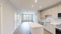 This well-appointed one-bedroom, one-bathroom residence at 412 Summer St in Abington, MA offers a thoughtfully designed layout with modern finishes throughout. The open-concept kitchen and living area serves as the heart of the home, featuring light wood cabinetry extending to the ceiling, a white quartz countertop island, a white tile backsplash, and a full suite of stainless steel appliances including a gas range, built-in microwave, dishwasher, and refrigerator. Warm hardwood-style flooring flows throughout the main living areas, adding a clean, contemporary feel. Large windows in the living space invite abundant natural light while providing views of the surrounding community. The bedroom is a comfortable retreat with plush carpeting, a window with an exterior view of greenery, and direct access to a spacious walk-in closet outfitted with wire shelving on multiple walls for ample storage. The full bathroom features hardwood flooring, a vanity with a light wood finish, and a glass-enclosed walk-in shower with white tile surround. Neutral gray tones on the walls complement the bright, modern aesthetic carried consistently throughout the entire space.