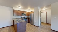 This single-floor, 2-bedroom, 1-bathroom unit offers a practical and comfortable layout designed to maximize every inch of its living space. The kitchen is a standout feature, showcasing warm medium-toned wood cabinetry, stone-look countertops with a mosaic tile backsplash, and a full suite of stainless steel appliances including an electric range, over-the-range microwave, and refrigerator. A peninsula with a double-basin sink adds additional prep space and separates the kitchen from the open living area. The living area features durable hardwood-style flooring that carries a warm, clean aesthetic throughout the main space, with a paneled entry door and access to a side window that brings in natural light.

Both bedrooms are carpeted for added comfort. The primary bedroom is a well-sized retreat with dual windows offering views of the surrounding greenery. The second bedroom includes a built-in closet with wire shelving, providing practical storage solutions. The shared bathroom is finished with stone-look tile flooring, a wood-toned vanity with a granite-style countertop, a large mirror with overhead lighting, and a tub-shower combination. A hallway connects the rooms cohesively, completing this efficiently designed and move-in-ready home.