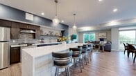 This thoughtfully designed single-floor unit offers a seamless open-concept layout connecting the kitchen, dining, and living areas into one cohesive, functional space. The kitchen is a standout feature, showcasing dark espresso cabinetry, a striking mosaic tile backsplash, quartz countertops, stainless steel appliances, and an expansive waterfall island with bar seating for four — illuminated by elegant pendant lights. The living room is bright and welcoming, featuring a tray ceiling with a modern chandelier, large windows, and a sliding glass door that opens to a private balcony overlooking lush tree canopy views. A separate dining area offers additional seating with natural light streaming in through a large window and direct balcony access. Throughout the unit, warm wood-tone luxury vinyl plank flooring provides a consistent and contemporary feel. The accessible bathroom is cleanly finished with large-format hexagonal marble-look tile flooring, full-height wall tile, and stainless grab bars. Recessed lighting and neutral tones throughout contribute to a polished, modern ambiance, while the open sightlines from the kitchen through to the living room maximize the sense of space and connectivity across the entire floor plan.
