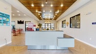 The Preserve's clubhouse and leasing facility is a thoughtfully designed single-story community hub offering a comprehensive range of amenities. At the heart of the space is a stylish reception area, distinguished by a warm wood-paneled ceiling with recessed and pendant lighting, a sleek multi-tiered front desk, and light hardwood-style flooring that carries throughout much of the building.

The fitness center is generously sized, featuring multiple treadmills, an elliptical, a stationary bike, and a full array of strength equipment. Large windows flood the room with natural light, while wall-mounted flat-screen TVs provide entertainment during workouts. A durable rubberized floor ensures safety and functionality.

A covered outdoor lounge extends the living space outside, furnished with plush navy-blue sofas and accent chairs atop a bold geometric rug, with views of the surrounding landscape providing a relaxing atmosphere. French doors connect this patio seamlessly to the interior.

Inside, a dedicated conference room offers a large worktable with ample seating, while the computer lab provides a row of desktop workstations beside wide windows with outdoor views. A well-appointed kitchenette serves the common areas, featuring dark cabinetry, granite countertops, stainless steel appliances, and a sink. Dual water fountains and accessible design elements reflect the facility's attention to inclusivity and convenience.