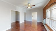 This single-floor space combines classic architectural character with functional design. The main living area is immediately distinguished by exposed red brick walls that frame large windows, filling the room with natural light. Rich, deep-toned hardwood floors run throughout, complementing the crown molding and ceiling fan with integrated lighting overhead. An arched doorway adds a subtle architectural detail, connecting the living space to the rest of the unit.

The bedroom area benefits from its own generous walk-in closet, equipped with built-in shelving and hanging rods, offering ample storage. Hardwood flooring continues into this space, maintaining visual continuity throughout.

The kitchen is well-appointed with white raised-panel cabinetry extending to the ceiling, granite-style countertops, a stainless steel sink, and hardwood flooring underfoot. Crown molding carries through here as well, providing a cohesive finishing detail.

The bathroom features a full soaking tub surrounded by clean white subway tile, creating a bright and timeless aesthetic. Overall, the space balances historic charm—evident in the exposed brick and hardwood floors—with updated finishes, resulting in a warm and characterful interior.