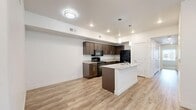 Located in Vineyard, Utah, this well-designed 3-bedroom, 2-bathroom single-floor residence offers a clean, modern aesthetic throughout. The open-concept kitchen serves as the heart of the home, showcasing rich dark wood cabinetry, granite-look countertops, black appliances, and a central island with a built-in sink and elegant pendant lighting overhead. Light wood-look LVP flooring extends seamlessly through the kitchen and living areas, creating a bright, cohesive feel.

The living room is generously proportioned, bathed in natural light from large windows and a glass exterior door that brings in additional brightness. Each bedroom features plush carpet flooring and windows that invite natural light. The primary bedroom stands out with its spacious walk-in closet, complete with full-length hanging rods and ample storage space. The secondary bedrooms are well-sized and similarly finished with soft carpeting and natural light.

Both bathrooms are appointed with LVP flooring, dark wood vanities with granite-look countertops, and a tub/shower combination. A connecting hallway with a dedicated closet adds practical storage. The overall design throughout is crisp and contemporary, with white walls, clean trim, and thoughtful finishes that create a comfortable, move-in-ready living environment.