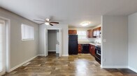 This single-floor unit offers a practical and comfortable layout designed for everyday living. The open living area is finished with warm, wood-look plank flooring that runs throughout the main areas, creating a cohesive and inviting atmosphere. A ceiling fan with light fixture adds both function and character to the space. French doors along one wall allow natural light to fill the room while providing access to the exterior. Adjacent to the living area, the kitchen is well-equipped with rich cherry-toned cabinetry extending to the upper walls for generous storage, complemented by a classic subway tile backsplash and light stone-finish countertops. Black appliances — including a gas range, refrigerator, and dishwasher — provide a bold contrast to the warm cabinetry. A stainless steel sink is positioned beneath a window, allowing natural light while cooking or cleaning. A dedicated laundry closet with washer and dryer hookups adds convenience. The bedroom is finished with plush grey carpeting, neutral walls, and a window that brings in soft natural light, creating a calm retreat. The full bathroom features wood-look flooring, a tub/shower combination with white tile surround, and a window for natural ventilation. Throughout, clean white trim and neutral tones contribute to a bright, move-in-ready environment.