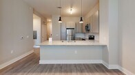 Located at 3915 William E Murray Blvd in Charleston, SC, this single-floor, 3-bedroom, 1-bathroom home offers a thoughtfully designed layout with contemporary finishes throughout. The open-concept kitchen serves as a central highlight, featuring stainless steel appliances, sleek light wood cabinetry, a textured tile backsplash, and a peninsula island topped with granite countertops. Stylish pendant lighting illuminates the space, while a ceiling fan provides comfort in the adjacent living area. Wood-look plank flooring flows seamlessly through the kitchen, hallway, and living areas, lending a clean, cohesive aesthetic. A well-lit hallway connects the main living space to the three bedrooms, framed by crisp white panel doors with matte black hardware. The bedrooms are carpeted for added warmth and comfort, with windows offering natural light and views of surrounding greenery. One bedroom includes a double closet, while the primary bedroom connects to a dedicated walk-in closet with wire shelving. The full bathroom is well-appointed with a granite-topped vanity, wood-toned cabinetry, and a tub-shower combination. Neutral warm-gray walls and consistent trim throughout give the home a polished, move-in-ready feel.
