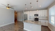 Located at 5840 Farrington Rd in Chapel Hill, NC, this single-floor unit offers a well-designed open layout with modern finishes throughout. The kitchen serves as a central highlight, featuring a large island with granite countertops and an undermount stainless steel sink illuminated by a trio of pendant lights. White shaker-style cabinetry extends to the ceiling, providing generous storage, while a subway tile backsplash adds a clean, classic detail. Stainless steel appliances, including a refrigerator, electric range, and over-the-range microwave, complete the space. Natural light enters through multiple windows fitted with horizontal blinds, brightening both the kitchen and surrounding living areas. Wood-look plank flooring runs throughout the main living spaces, offering durability and a cohesive aesthetic. The bedrooms feature neutral-toned carpet and windows that bring in additional natural light. Both bathrooms are finished with granite-topped white vanities, tub-shower combinations with white tile surrounds, and brushed nickel fixtures, along with wood-look flooring. A dedicated in-unit laundry area accommodates a full-sized washer and dryer with overhead wire shelving for additional storage. The overall palette of soft grays and whites creates a clean, contemporary ambiance throughout.