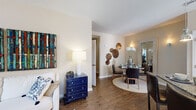 Located in Deerwood Village in Ocala, Florida, this single-floor residence offers a thoughtfully designed open-concept layout that seamlessly connects the main living areas. Rich wood-style flooring flows throughout the living, dining, and kitchen spaces, creating a warm and cohesive aesthetic.

The living room is bright and inviting, with neutral walls that complement bold decorative accents. It opens directly to a well-defined dining area, which features a wall sconce and access to natural light via a large mirror that amplifies the sense of space.

The kitchen is a standout feature, boasting white cabinetry, a subway tile backsplash, stainless steel appliances including a range and microwave, and a granite-topped breakfast bar with seating. Pendant lighting and a track-light fixture add both function and style. A transom window above the front entry fills the entryway with natural light.

The bedroom offers plush carpeting, generous windows dressed with vibrant drapes, and a walk-in closet with built-in shelving. The en-suite bathroom is finished with granite countertops, white cabinetry, a large vanity mirror, and a separate soaking tub and shower area. A second full bathroom mirrors the same quality finishes. This residence delivers comfort and modern style in a complete single-level layout.