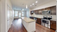 Located at 500 Chris Kelley Blvd in Hutto, TX, this well-appointed one-bedroom, one-bathroom unit offers a thoughtfully designed layout across a single floor. The open-concept kitchen and living area serves as the heart of the space, showcasing rich dark-wood cabinetry, a striking granite-topped center island with pendant lighting overhead, and a full suite of stainless steel appliances including a refrigerator, range, microwave, and dishwasher. A tile backsplash and recessed lighting add polished finishing touches, while warm hardwood-style flooring extends throughout the main living area, enhancing the sense of openness. Large windows at the far end of the living space invite natural light and provide outdoor views, complemented by a ceiling fan for added comfort. The bedroom offers plush carpeting, a ceiling fan, and a generously sized window that frames pleasant outdoor scenery, creating a calm and restful retreat. The bathroom is finished with neutral tile flooring, a granite vanity with dark wood cabinetry, a framed mirror, and a full tub-shower combination with tile surround. Clean lines, neutral tones, and consistent finishes throughout give the space a cohesive and modern aesthetic.