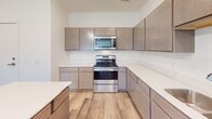 Located at 112 Fifth St NE in Faribault, Minnesota, this single-floor unit offers a clean, contemporary design throughout. The open kitchen is a standout feature, equipped with stainless steel appliances including a range, microwave, dishwasher, and refrigerator, complemented by warm taupe flat-front cabinetry, white countertops, and light wood-style flooring. A kitchen island provides additional workspace and casual dining space. The living area is bright and open, featuring the same light wood-style flooring and a sliding glass door that invites natural light and provides outdoor access. The bedrooms are carpeted and bathed in natural light through generous windows, offering views of the surrounding landscape. Built-in closets provide practical storage. The primary bathroom is generously sized, featuring a dual-sink vanity with ample cabinetry, white countertops, tile-style flooring, and accessible safety grab bars, reflecting a thoughtful, accessibility-conscious design. Throughout the unit, a neutral white and warm beige color palette creates a bright, cohesive, and move-in-ready atmosphere suited for comfortable everyday living.