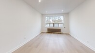 This thoughtfully laid-out 1-bedroom, 1-bathroom unit offers a clean, modern aesthetic throughout its single floor. Light-toned hardwood flooring flows seamlessly across all rooms, creating a bright and cohesive atmosphere. The entry hallway provides a welcoming transition into the main living areas, with clean white walls and efficient use of space.

The living room is generously proportioned, featuring recessed lighting and a large window fitted with a classic cast-iron radiator, flooding the room with natural light and views of the surrounding neighborhood. Adjacent to the living area, the kitchen is well-equipped with white shaker-style cabinetry extending to the ceiling, a white subway tile backsplash, stainless steel appliances including a range, over-the-range microwave, and refrigerator, as well as a window that brings in additional natural light.

The bedroom offers a comfortable footprint, complete with a built-in closet, a large window with a radiator beneath it, and the same light hardwood flooring found throughout. The bathroom features a full tub-shower combination with white subway tile surround, a vanity with sink, and a clean, functional design. A dedicated hallway connects all rooms efficiently, completing this practical and stylish layout.