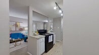 This single-story, 2-bedroom, 2-bathroom residence offers a thoughtfully designed layout that makes efficient use of its space. Light wood-style flooring flows throughout the main living areas, complementing the neutral gray walls and creating a clean, modern aesthetic.

The kitchen is equipped with black appliances, including a range and refrigerator, set against white cabinetry and granite-look countertops. A peninsula with bar seating opens directly to the living and dining area, enhancing the social flow of the space. Track lighting illuminates the kitchen, while a hallway beyond provides access to in-unit laundry connections.

The open-concept living and dining area benefits from a large sliding glass door that invites natural light and offers views of the outdoor patio area. The space is versatile enough to accommodate both a seating arrangement and a dining table.

The primary bedroom is generously sized, featuring plush carpet, a ceiling fan, and direct access to a private en-suite bathroom. The second bedroom also features carpet flooring and ample room for furnishings. Both bathrooms include granite-look vanity countertops and tub-shower combinations. The unit also includes two closets and a connecting hallway, providing practical storage throughout.