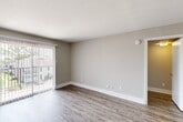 This well-appointed one-bedroom, two-bathroom unit at 8797 Hammerly Blvd in Houston, TX offers a thoughtfully designed single-floor layout. The combined kitchen and living area serves as the heart of the home, with the kitchen showcasing white shaker cabinetry with brushed gold hardware, light granite-style countertops, stainless steel appliances including a dishwasher and range, and a deep basin sink. Wood-style luxury vinyl flooring runs throughout the main living areas, lending a clean and contemporary feel. The open living room is bright and airy, featuring neutral gray walls, large windows with vertical blinds, and a sliding glass door that opens to a private patio, inviting natural light throughout the day. A hallway connects the main living space to the private quarters. The bedroom is a comfortable retreat, finished with plush wall-to-wall carpeting, a large window with outdoor views, and access to a dedicated closet. The two bathrooms provide added convenience, with one featuring a full tub-shower combo with brushed nickel fixtures. Clean lines, neutral tones, and wood-style flooring in the hallway tie the entire space together for a cohesive, modern aesthetic.