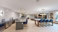 Located at 1850 Glenview Rd in Glenview, Illinois, this generously sized single-floor community living space is thoughtfully designed to accommodate a variety of social and leisure activities. Light-toned hardwood flooring runs throughout, complementing the warm neutral palette of the walls and creating a bright, welcoming atmosphere enhanced by recessed lighting.

The space is organized into several distinct functional zones. A central lounge area features a tiled fireplace framed by a slatted wood accent wall with open shelving, paired with comfortable upholstered seating and direct access to an outdoor patio through sliding glass doors. Adjacent to this, a formal dining area offers a long white table with bold navy upholstered chairs beneath elegant globe pendant lighting. A fully equipped bar counter with white subway tile backsplash, dark cabinetry, and navy bar stools serves as a social centerpiece, while an antique mirror-paneled wall adds depth and sophistication nearby. A billiards table occupies its own dedicated corner, and intimate seating clusters with accent chairs and gold side tables are positioned throughout for more private conversation. Curated wall art and decorative accessories complete the polished, contemporary aesthetic of this versatile gathering space.