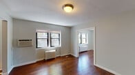 Located at 1213 Hawthorne Ave in the heart of Minneapolis, MN, this single-floor residence combines classic architectural character with modern updates throughout. Rich, dark hardwood floors flow seamlessly across the living spaces, lending warmth and continuity to the open layout visible in the 3D floorplan. Multiple rooms are illuminated by an abundance of natural light streaming through large, black-framed windows that frame views of surrounding greenery. Classic cast-iron radiators are present throughout, nodding to the building's heritage while providing reliable heating. A charming French door leads into one of the rooms, adding an elegant architectural detail. The kitchen is a standout feature, equipped with dark wood cabinetry, light quartz countertops, stainless steel appliances including a gas range and built-in microwave, and a crisp white subway tile backsplash that ties the space together with a clean, modern aesthetic. The bathroom continues the subway tile theme, featuring a full tub-shower combination surrounded by white tile, a window for natural light and ventilation, and a white vanity with medicine cabinet. The entryway offers a welcoming transition into the home, with easy access to the kitchen. Throughout, neutral gray walls provide a versatile backdrop, making this a functional and inviting living space.