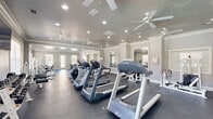 Located at 7601 Vestal Blvd in North Little Rock, Arkansas, this fitness center offers a generously sized, single-floor exercise space designed to accommodate a comprehensive workout experience. The room features durable dark rubber flooring throughout, providing a practical and resilient surface suited for a wide range of physical activities.

The space is outfitted with an impressive array of equipment, including multiple treadmills and elliptical machines arranged along one side for dedicated cardio training. A well-stocked dumbbell rack with a full range of free weights, accompanied by an adjustable bench, anchors the strength training area. Additional cable and resistance machines line the perimeter, supporting a variety of targeted muscle group exercises.

Natural light filters in through multiple large windows fitted with blinds, creating a bright and welcoming atmosphere. Several ceiling fans are strategically positioned throughout the room to ensure consistent airflow and comfort during workouts. Recessed lighting supplements the natural light for well-distributed illumination at all hours.

Crown molding and clean white trim details lend a polished, finished aesthetic to the space. Large wall mirrors reflect the room's depth, enhancing the sense of openness. A wall-mounted flat-screen television provides entertainment for cardio sessions. The overall design is clean, functional, and thoughtfully organized to support both cardio and strength training needs.