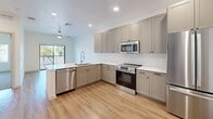 Located at 1225 North Arizona Avenue in Gilbert, AZ, this thoughtfully designed one-bedroom, one-bathroom residence offers a clean, modern aesthetic across a single floor. The open-concept layout creates a seamless flow between the living and kitchen areas, maximizing the efficient use of space.

The kitchen is a standout feature, showcasing gray shaker-style cabinetry with matte black hardware, white quartz countertops, a subway tile backsplash, and a full suite of stainless steel appliances including a French door refrigerator, electric range, built-in microwave, and dishwasher. Light wood-tone flooring runs throughout the main living areas, adding warmth to the modern palette.

The bedroom is a comfortable retreat with plush carpeting, crisp white walls, and a ceiling fan with a gold-toned fixture. A broad window invites natural light and provides outdoor views of the surrounding greenery. A dedicated closet offers practical storage.

The bathroom continues the home's contemporary design with a long dual-sink vanity featuring gray cabinetry, a backlit mirror, white quartz countertops, light wood flooring, and a soaking tub with white tile surround. The overall ambiance throughout the residence is bright, clean, and modern, reflecting a cohesive design sensibility suited for comfortable everyday living.