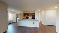 Located at 2555 Bella Colla Lane in Richland, Washington, this single-floor unit offers a well-designed, functional layout with a cohesive neutral color palette throughout. The open-concept kitchen anchors the living space, featuring rich dark-wood cabinetry, black appliances including a refrigerator, range, and microwave, and a generous peninsula island with a sink and counter seating — ideal for casual dining or meal prep. Track lighting illuminates the kitchen, while durable wood-style flooring flows seamlessly through the main living areas. The spacious living room receives natural light through sliding glass doors that open to an outdoor patio, enhancing the sense of openness. Two well-proportioned bedrooms offer carpeted flooring, ceiling fans, and closet storage. One bedroom features a large window with scenic views of the surrounding landscape. The unit includes two bathrooms, each finished with dark wood vanities and wood-style flooring — one with a tub/shower combination. A dedicated in-unit laundry area with a washer and storage shelving adds everyday convenience. Clean lines, neutral tones, and practical finishes define the overall aesthetic of this thoughtfully laid-out Richland residence.